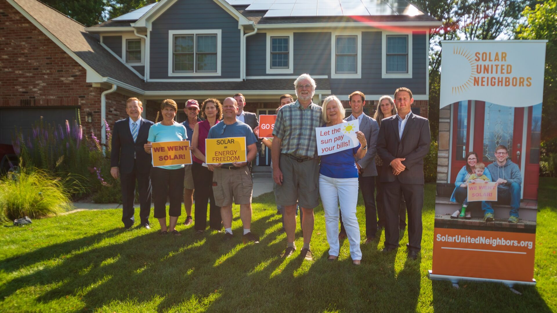 A group of solar supporters stand in front of a home with solar panels on the roof.