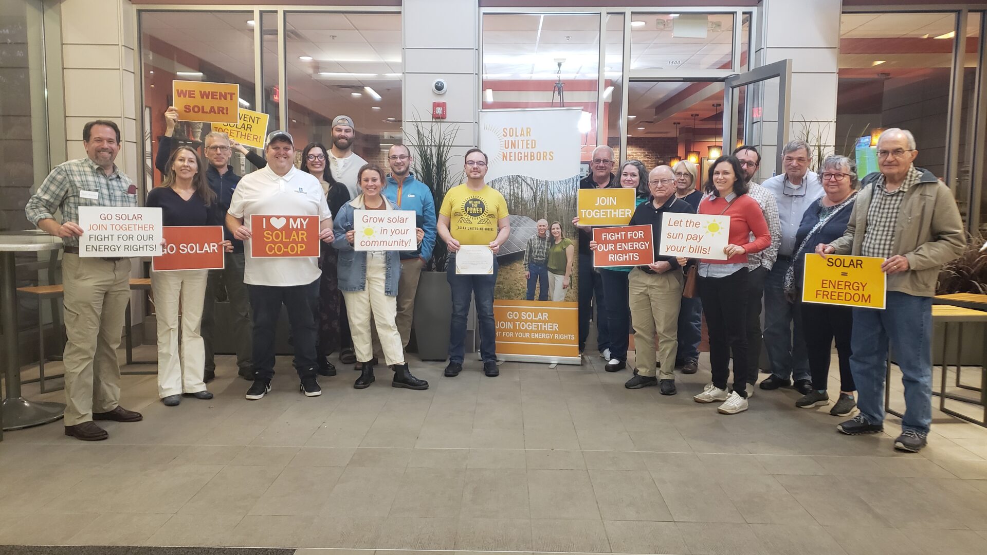 A group of solar supporters stand together holding signs about their solar co-op.