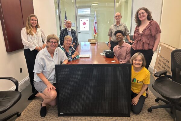 a group of 8 people in a state capitol with a plug-in solar panel