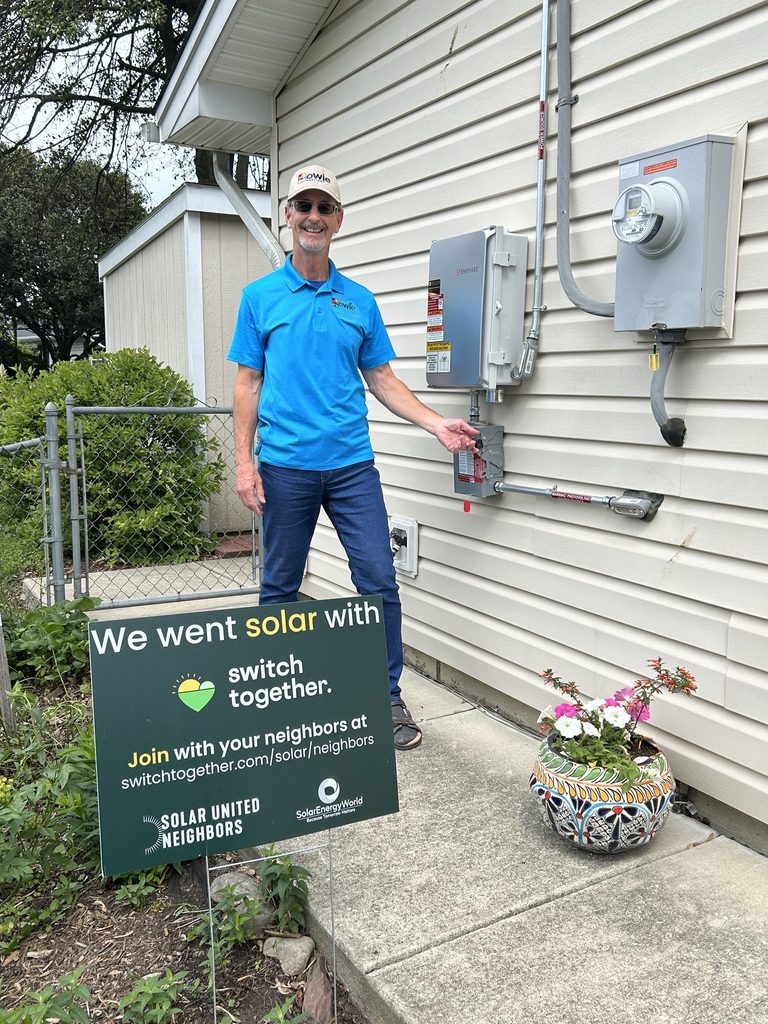 Bob Kellaway smiling in front of his battery and a Switch Together sign in his yard.